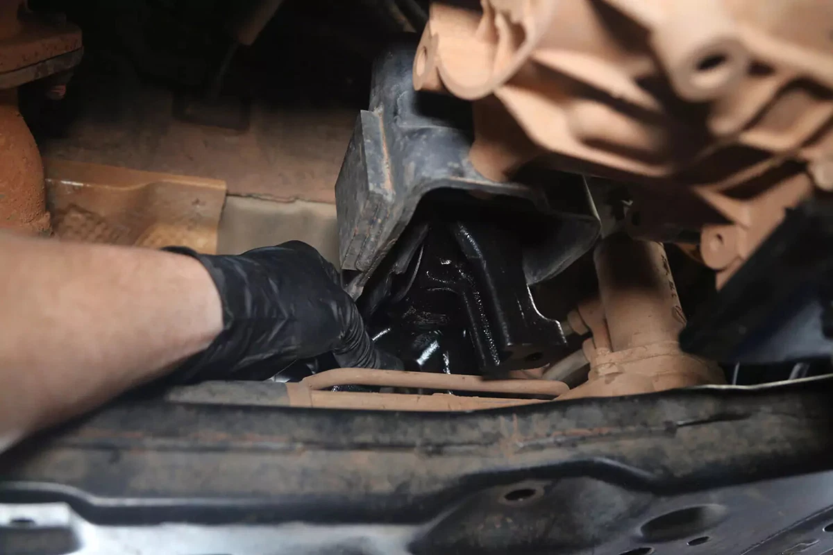 A mechanic with a black glove installs a new transmission mount.