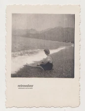 Curvy Older Woman in Swimsuit Sitting Alone On Pebble Beach Facing The Sea Photo