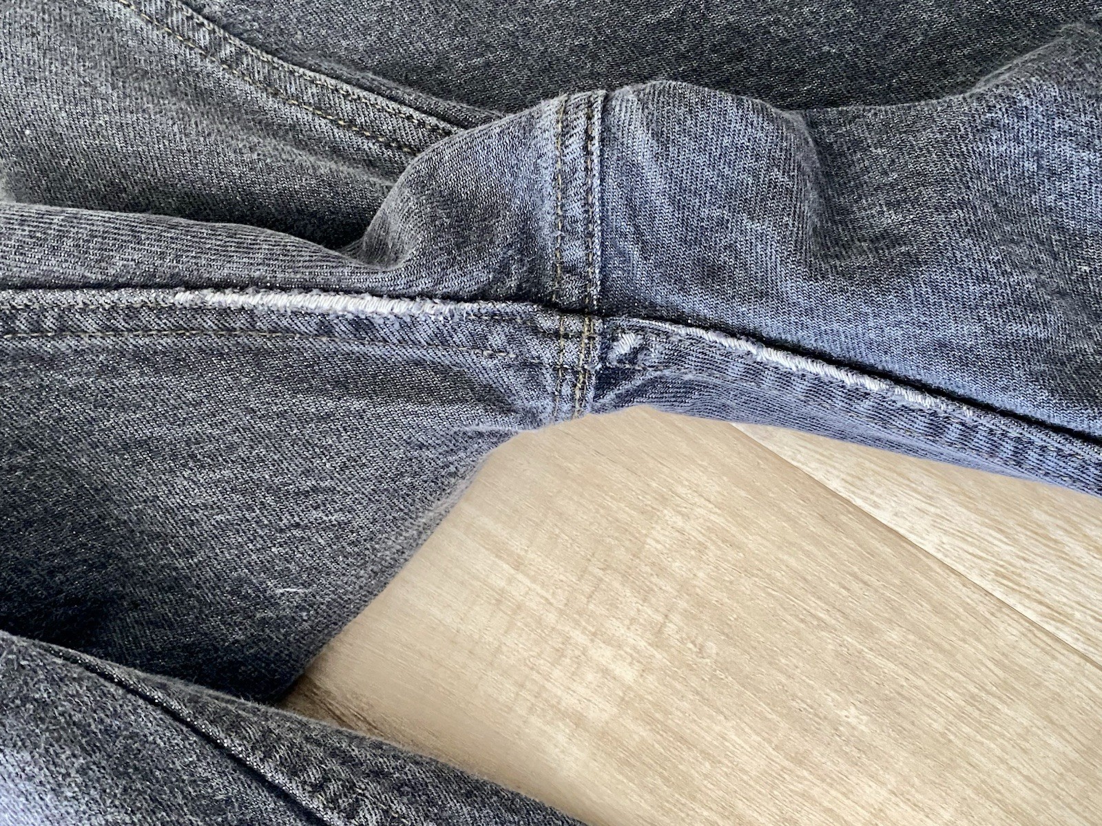 Close-up of a worn gray Levi’s 501 XX fly closure with visible stitching and buttoning, laid flat on light wood floor.