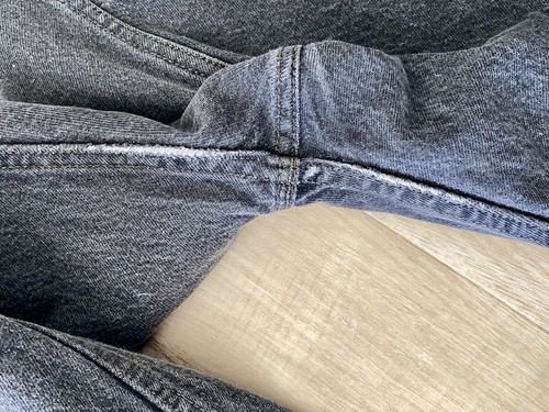 Close-up of a worn gray Levi’s 501 XX fly closure with visible stitching and buttoning, laid flat on light wood floor.