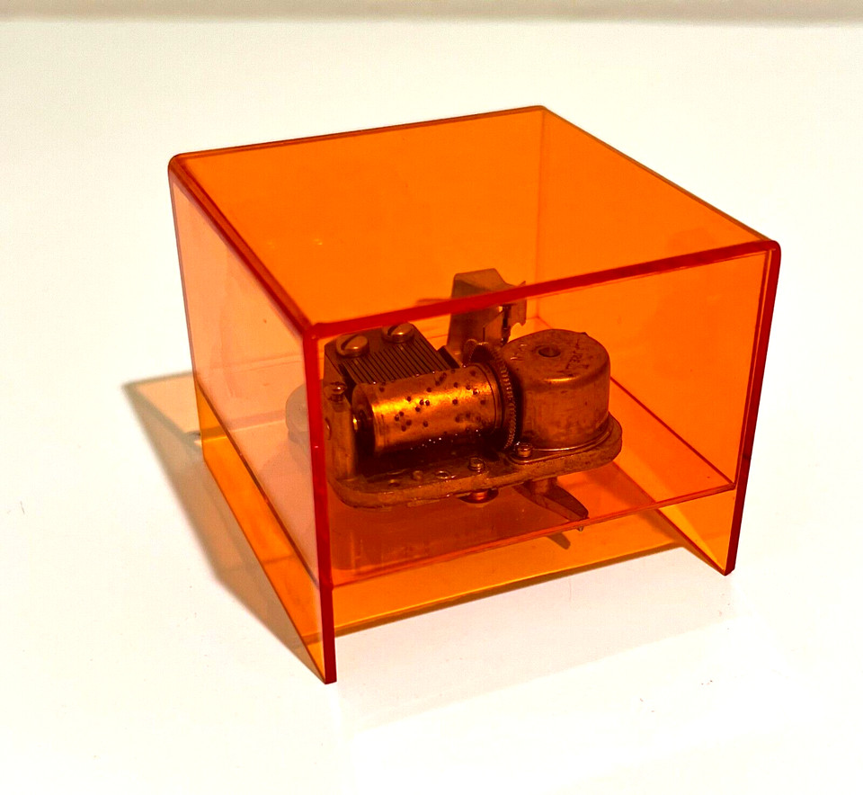 A see-through orange plastic Laurel Japan wind-up music box — rare mid-century design where you can literally watch the mechanism spin, like retro kinetic art.