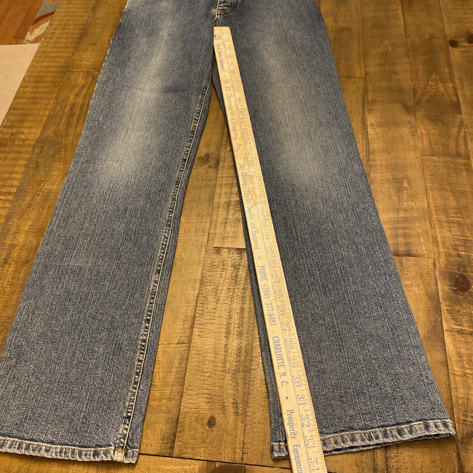 Blue Theory jeans, 30x33, with yellow measuring tape across the waistband, on wooden floor.
