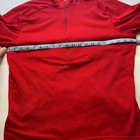 Red mesh Izumi men’s cycle shirt, small size, with yellow trim, made in USA, shown on hanger against measuring tape.