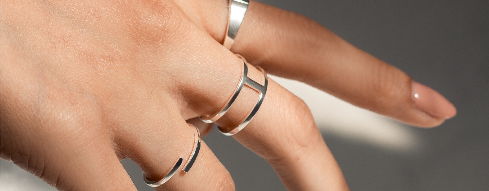 Nahaufnahme einer Hand mit minimalistischen Silberringen in modernem Design, betont durch weiches Licht.