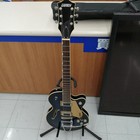 Black GRETSCH G5655T-QM hollow body electric guitar with silver hardware and three pickups, displayed on a dark blue stand.