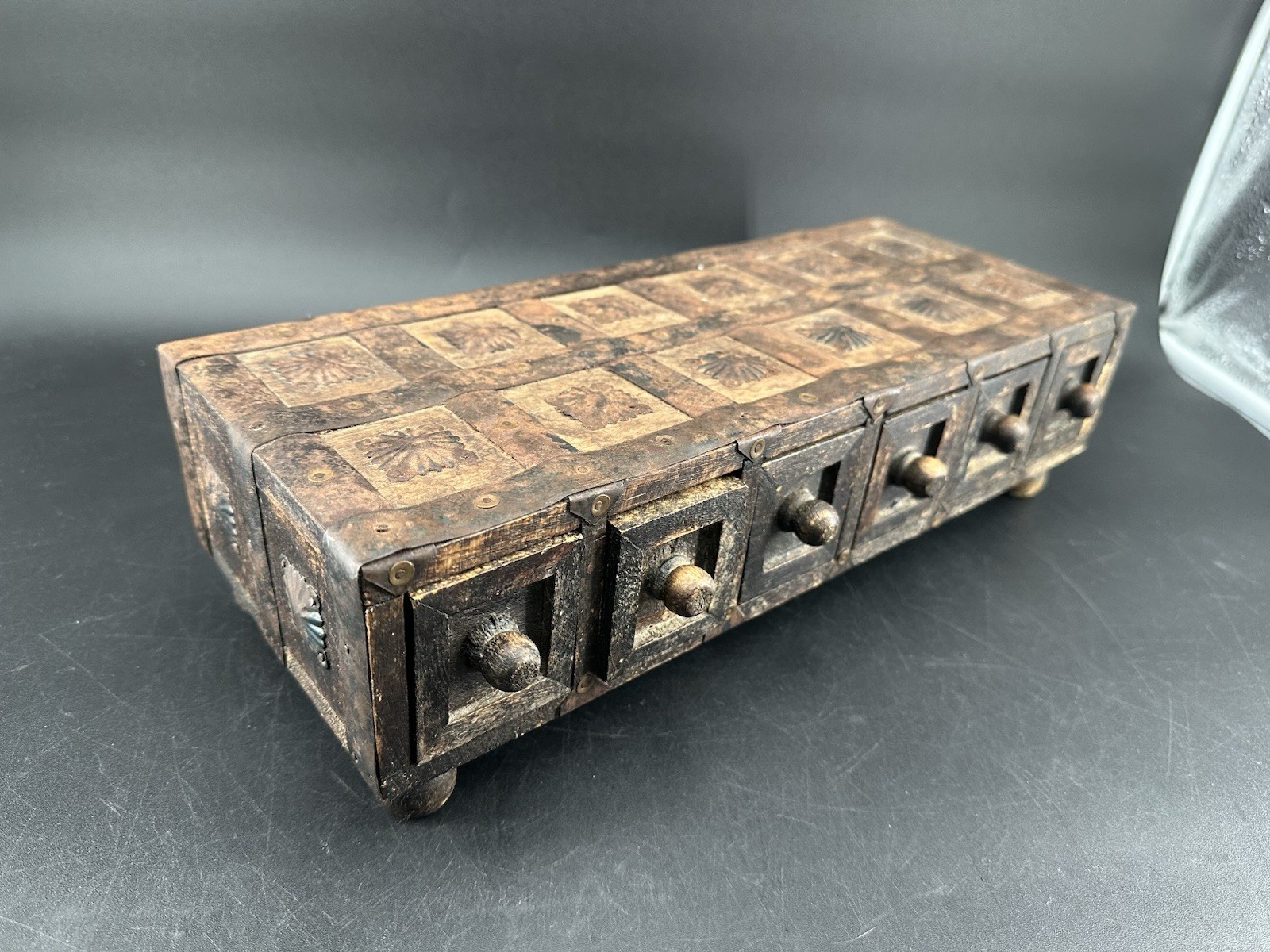 A carved wood apothecary-style box with six small drawers and hammered metal accents.
