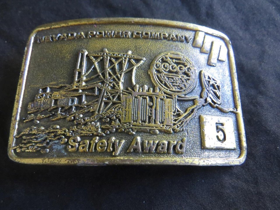 A brass belt buckle awarded by the Nevada Power Company for safety — weirdly specific corporate Americana that's become a legitimate piece of collectible kitsch.