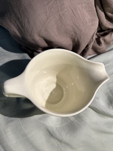White ceramic bowl with subtle floral print, made in Homer Laughlin, resting on a bed with dark fabric overhead.