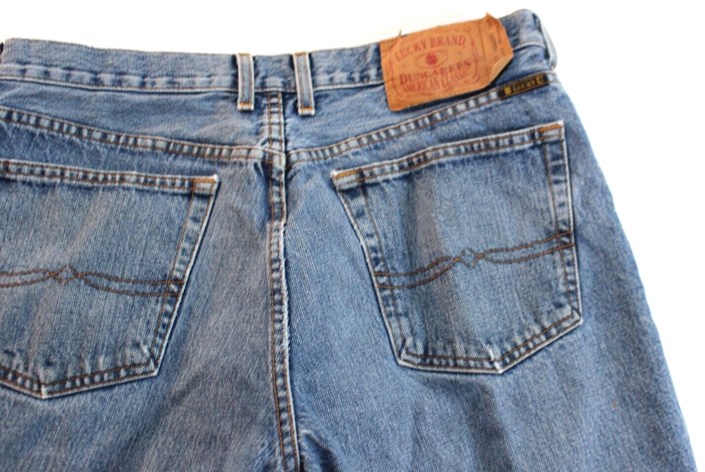 Back view of VTG Lucky Brand jeans in medium wash brown with paint splatter on right leg and tan leather patch on waistband.