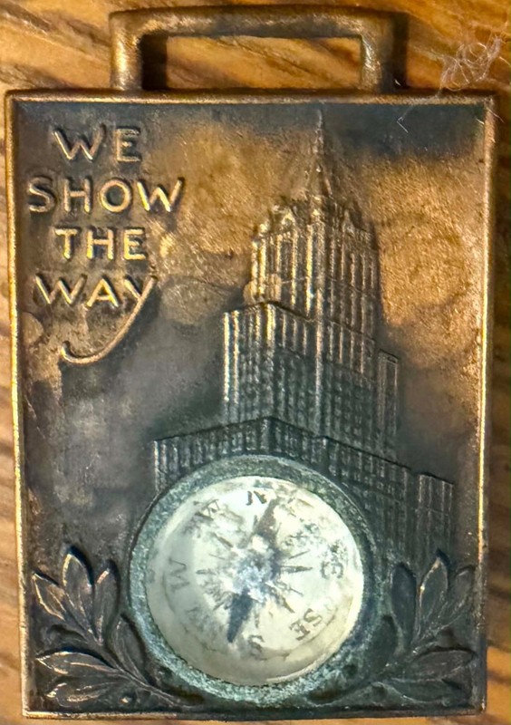 Watch fob: 1930s compass; "WE SHOW THE WAY"; Art Deco skyscraper (Lot #372)