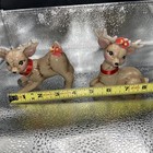 Pair of vintage Christmas reindeer babies, one lying on silver surface with red collar, one standing with floral headpiece.