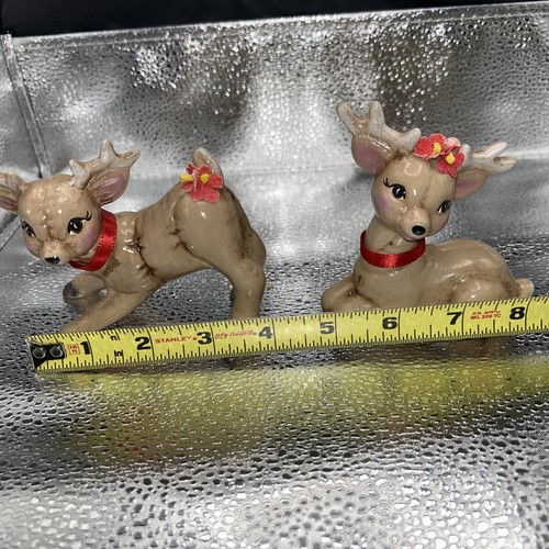 Pair of vintage Christmas reindeer babies, one lying on silver surface with red collar, one standing with floral headpiece.