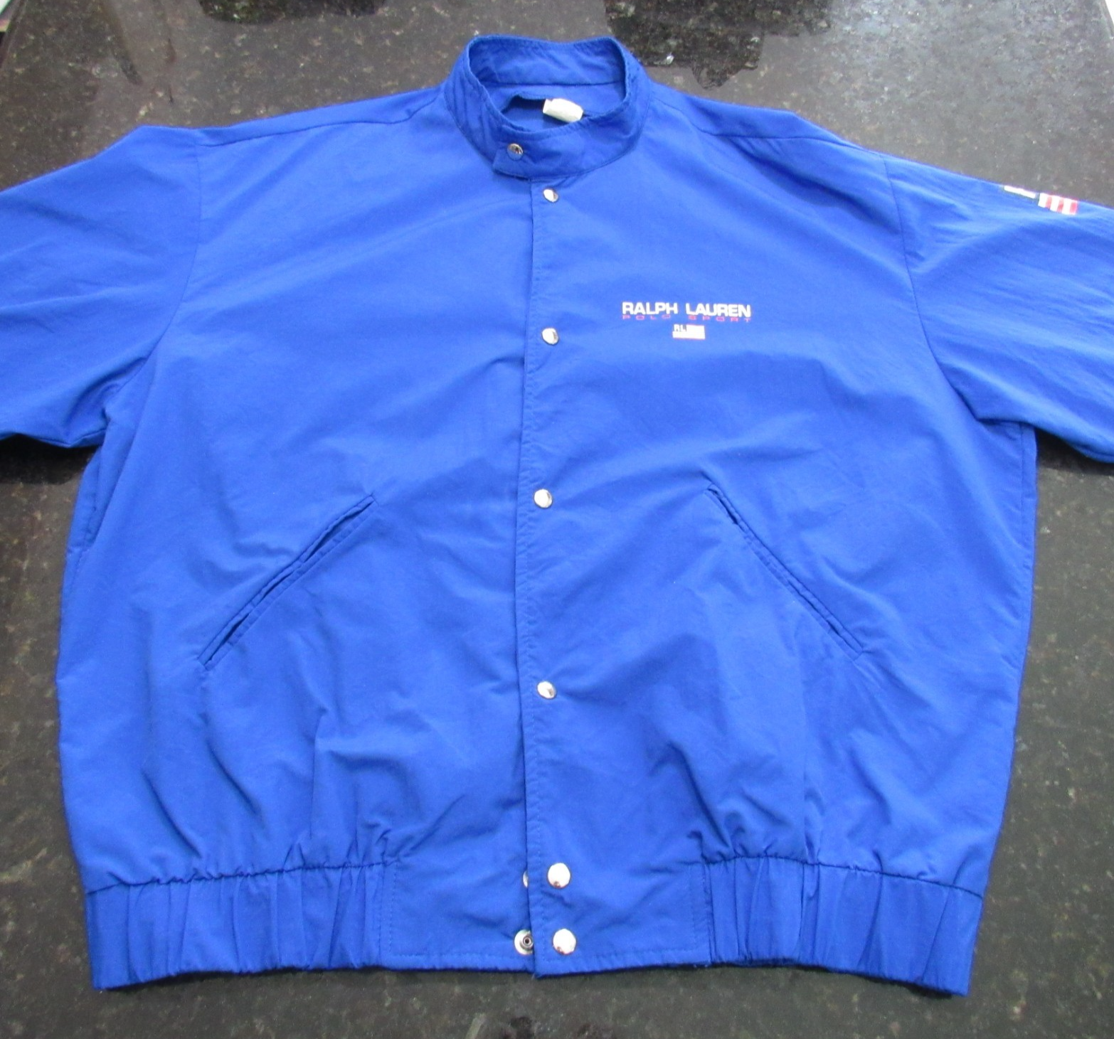 Blue Vtg 90s Polo Sport Ralph Lauren jacket with white snap buttons, pointed collar, and visible “Ralph Lauren” text.