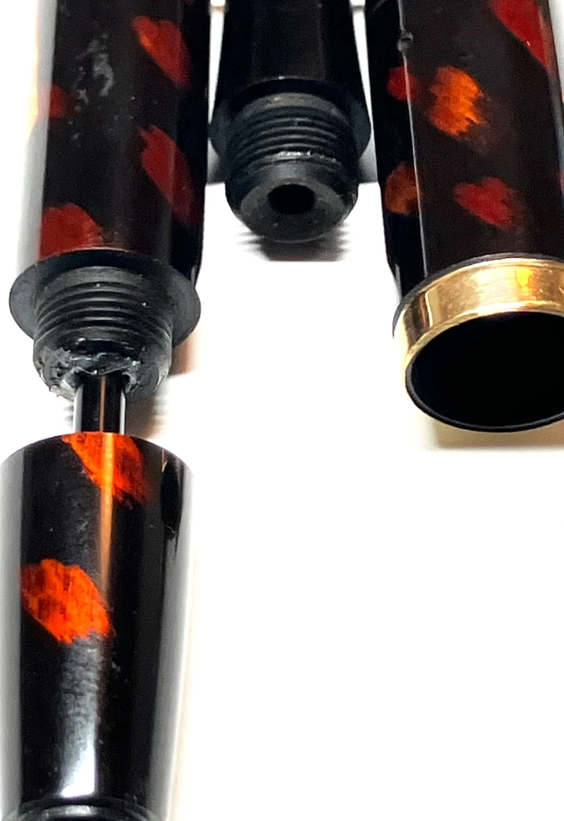 Black vintage fountain pen with orange ink shut off, resting on white paper with gold kokeshi label.