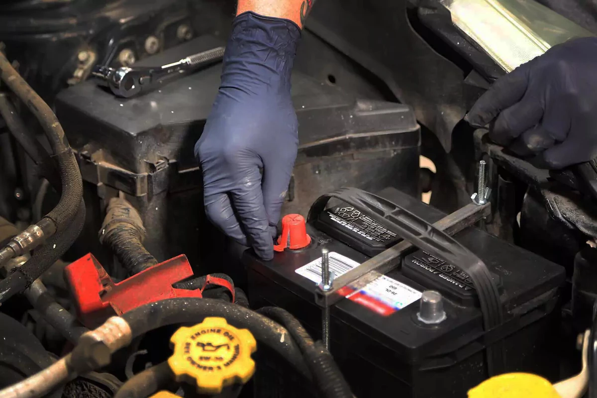 Pulling a red cap off a car battery terminal post.