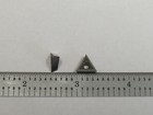 Small metal TT-221 carbide insert with triangular cutting head, shown beside a ruler on a gray surface.