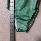Green Destira gymnastics leotard with gold glitter hologram, white trim, and adjustable straps, shown beside a metal ruler.