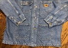 Blue denim Carhartt C59 chore coat with front button closure, two chest flap pockets, and visible Carhartt logo patch.