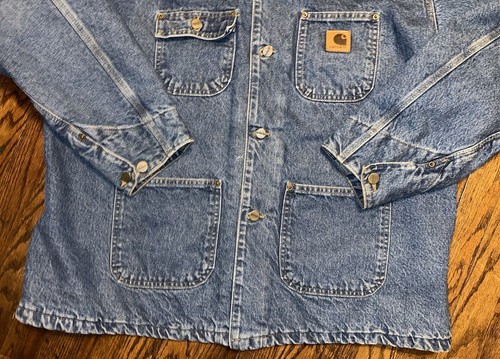 Blue denim Carhartt C59 chore coat with front button closure, two chest flap pockets, and visible Carhartt logo patch.