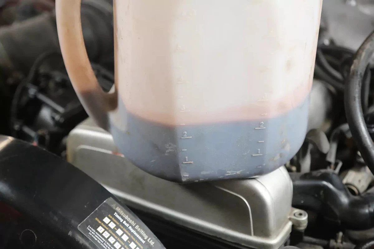 A clear plastic container holding power steering fluid that has been flushed out of a vehicle.