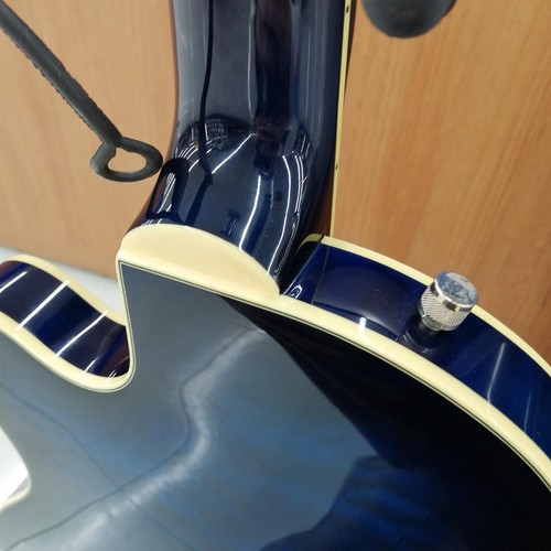 Hollow body electric guitar with dark blue finish, cream edge, and silver hardware against a light wood background.