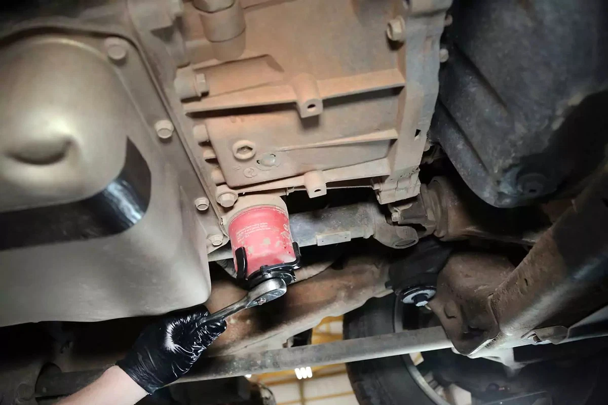 A mechanic removes the external automatic transmission filter with a socket wrench.