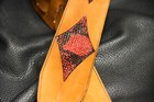 Black leather guitar strap with red and black diamond inlay on textured black background.