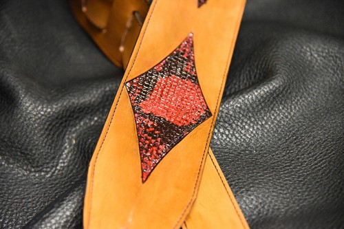Black leather guitar strap with red and black diamond inlay on textured black background.