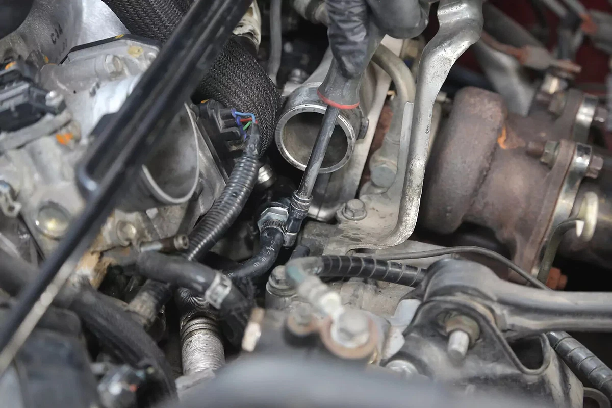 A mechanic wearing a black glove tightens a worm-gear clamp around the hose connected to the PCV valve.