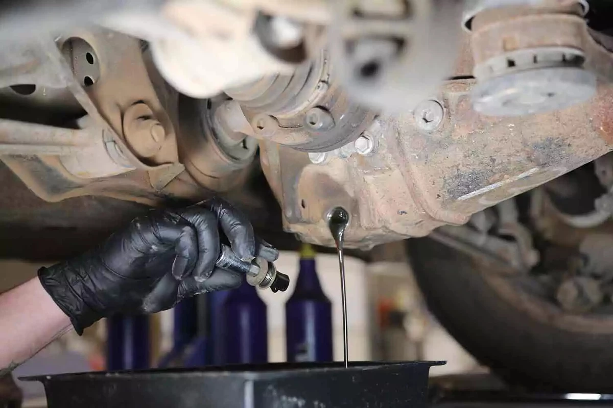 Differential fluid drains from a vehicle after a mechanic removes the drain plug.