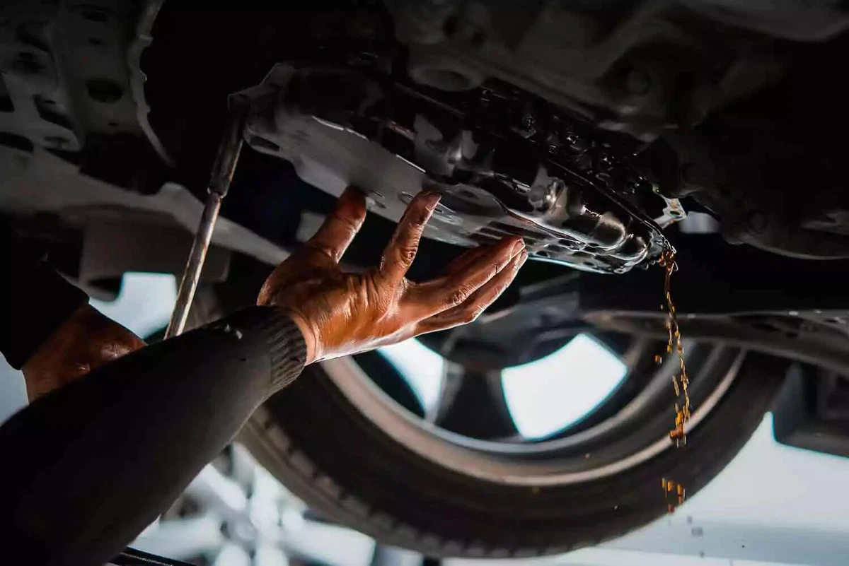 A mechanic draining transmission fluid by tilting the transmission pan forward after unbolting it.