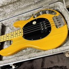 Yellow Sterling by MUSICMAN Ray 24 CA electric bass guitar with black pickguard, silver hardware, and four-on-the-floor strings in padded hard case.