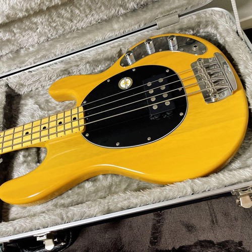 Yellow Sterling by MUSICMAN Ray 24 CA electric bass guitar with black pickguard, silver hardware, and four-on-the-floor strings in padded hard case.
