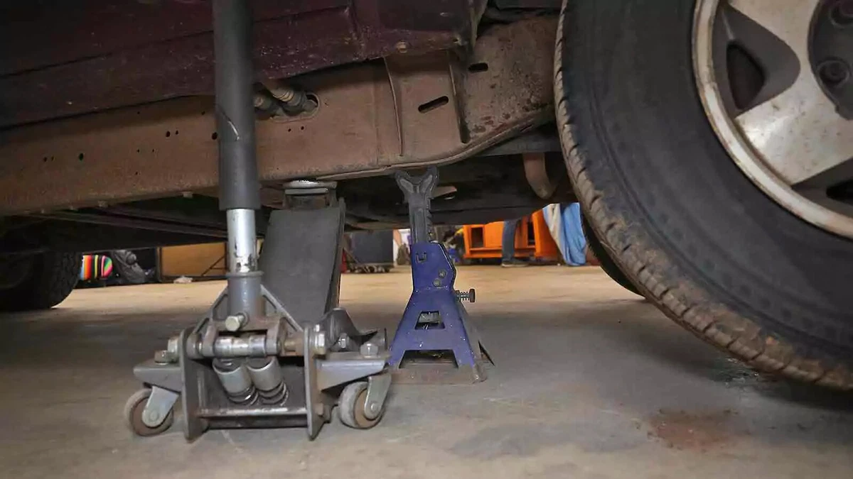 A truck raised with a floor jack and a jack stand on a concrete floor.