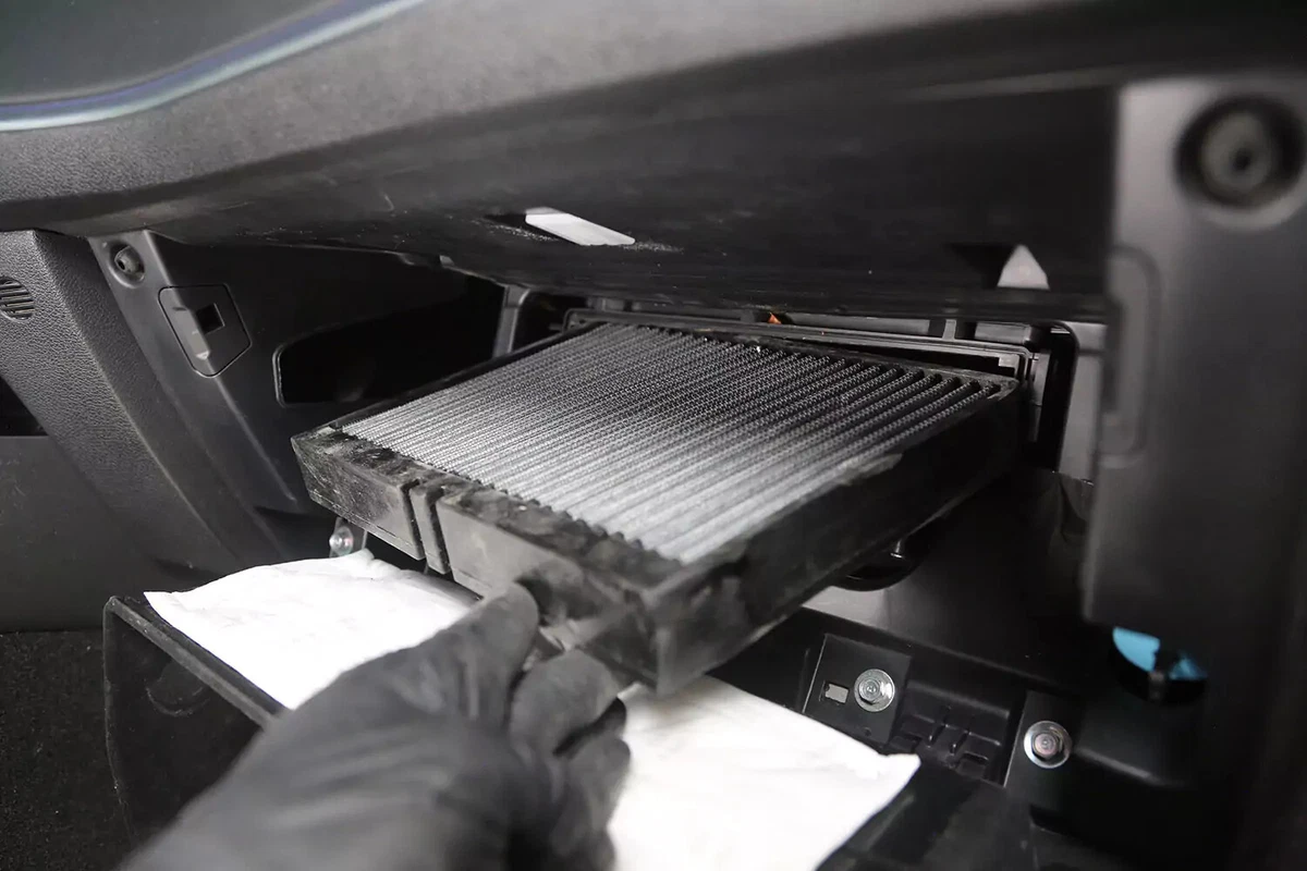 A mechanic wearing a black glove slides the new cabin air filter into place.