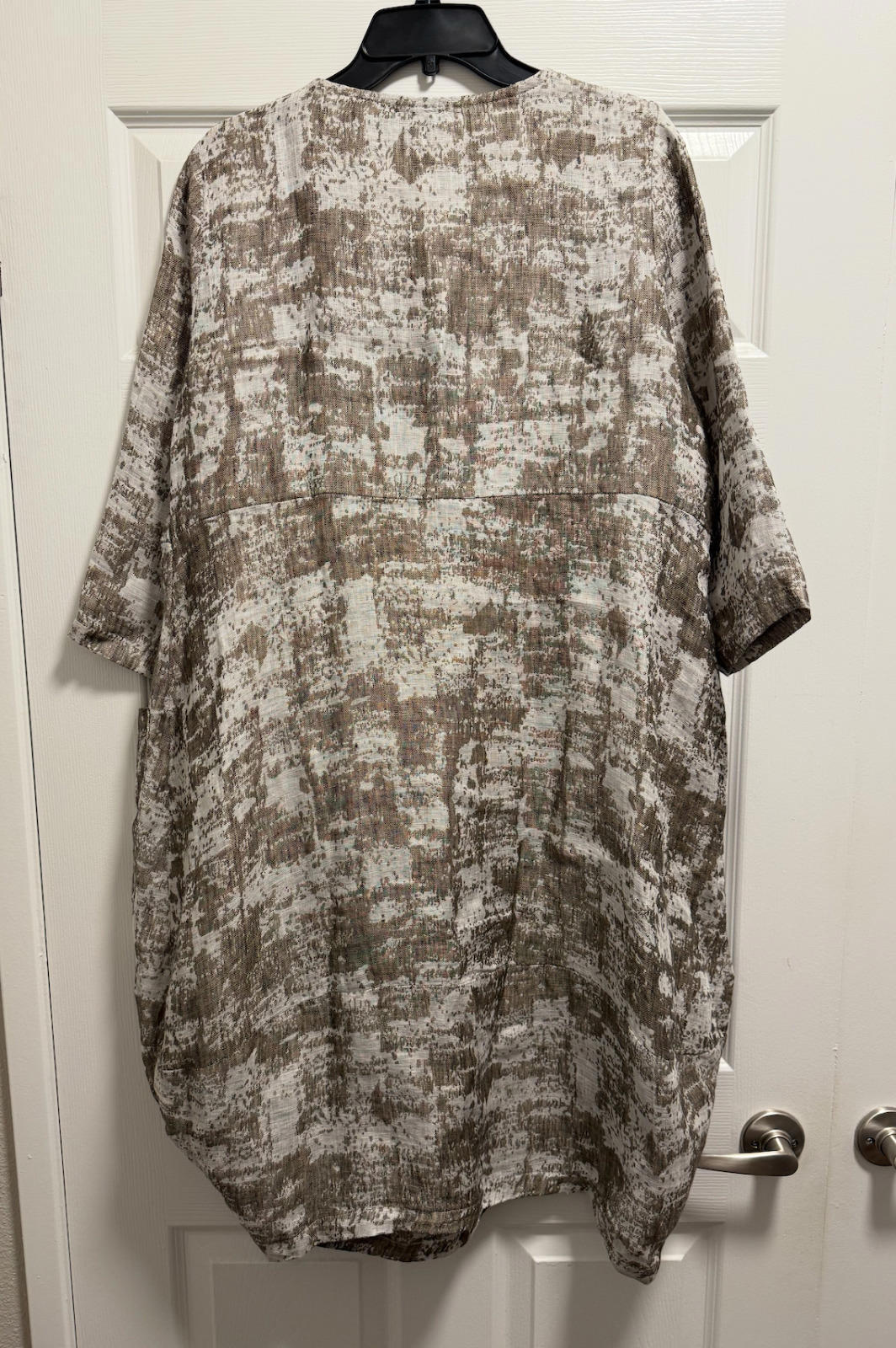 Chalet et Ceci green linen long sleeve dress with back tie waist, displayed on black hanger against white door.