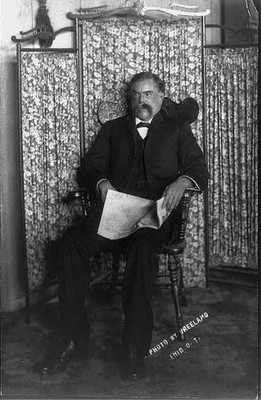 [David E. George, full-length portrait, seated, facing left, holding newspaper]
