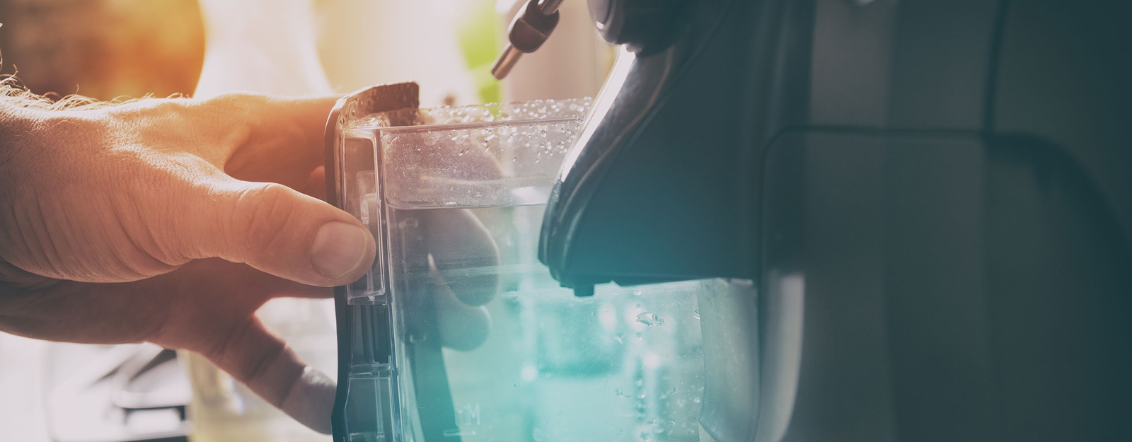 Jemand setzt einen Wasserauslauf in die dafür vorgesehene Vorrichtung eines Kaffeevollautomaten ein.
