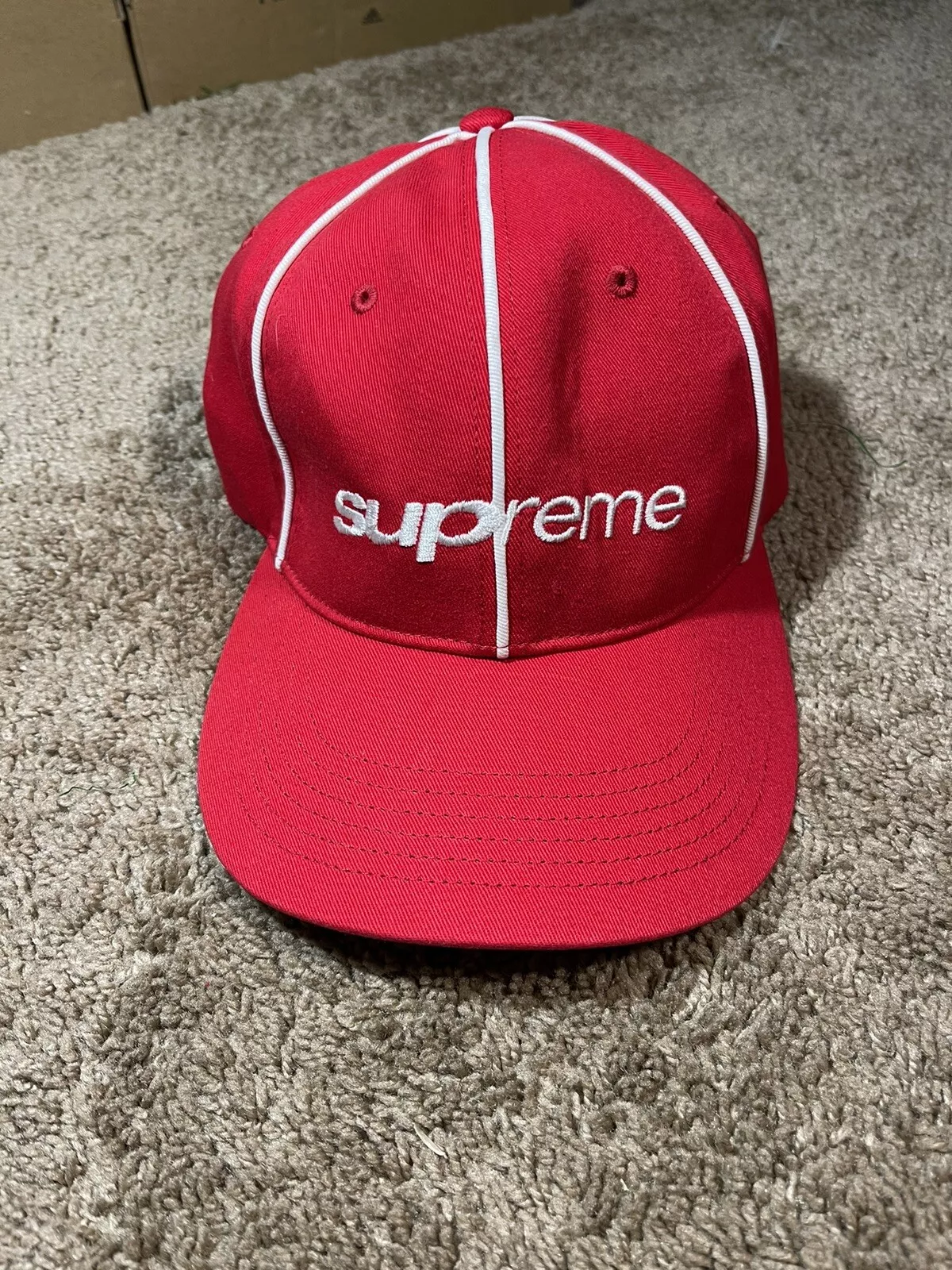 Chapeau Supreme Piping 6 panneaux FW22 neuf dans son sac rouge à la main