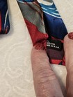 Red necktie with blue and gray abstract swirl pattern, black tag reading “Made in U.S.A.” on white fabric.