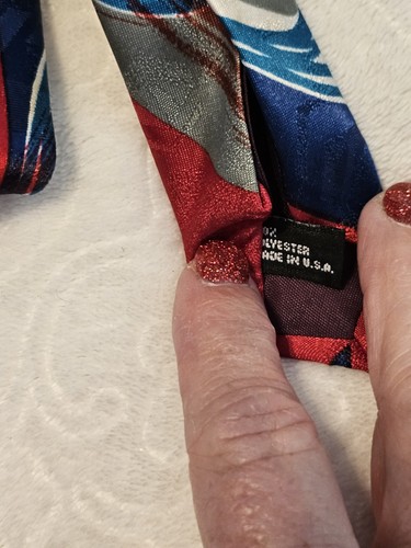 Red necktie with blue and gray abstract swirl pattern, black tag reading “Made in U.S.A.” on white fabric.