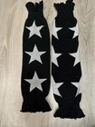 Black knit leg warmers with three white star patterns, long cuffs, and ankle-length design on wooden floor.