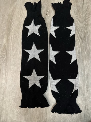 Black knit leg warmers with three white star patterns, long cuffs, and ankle-length design on wooden floor.