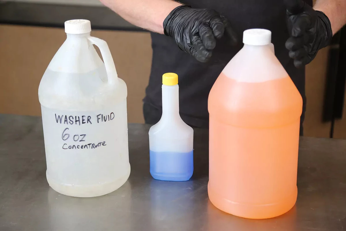 A clear jug of distilled water, a bottle of blue windshield fluid concentrate, and a jug of pre-mixed orange windshield fluid.