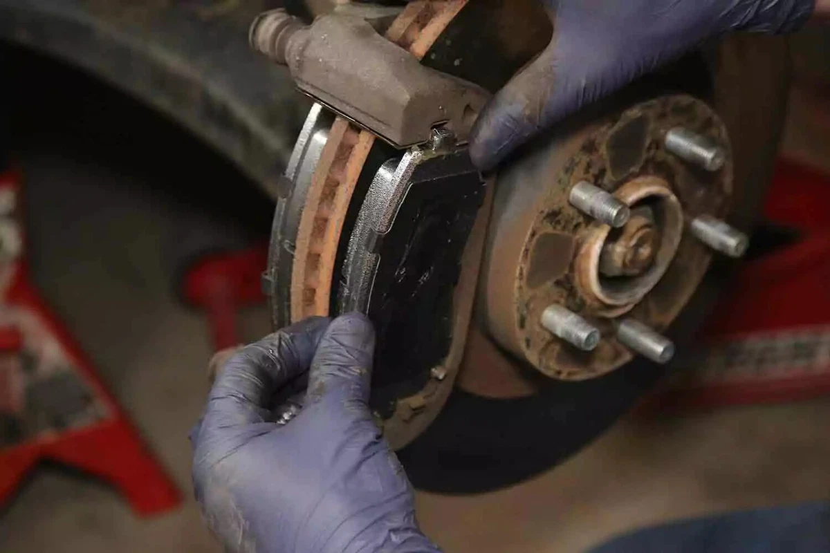 A mechanic wearing blue gloves checks the thickness of a vehicle's brake pads.