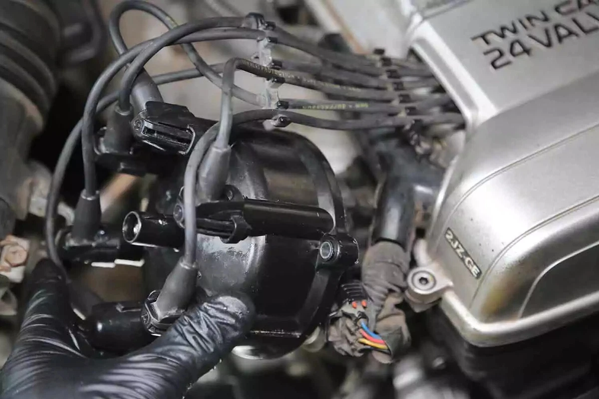 A mechanic wearing black gloves installs a new distributor cap in a vehicle.