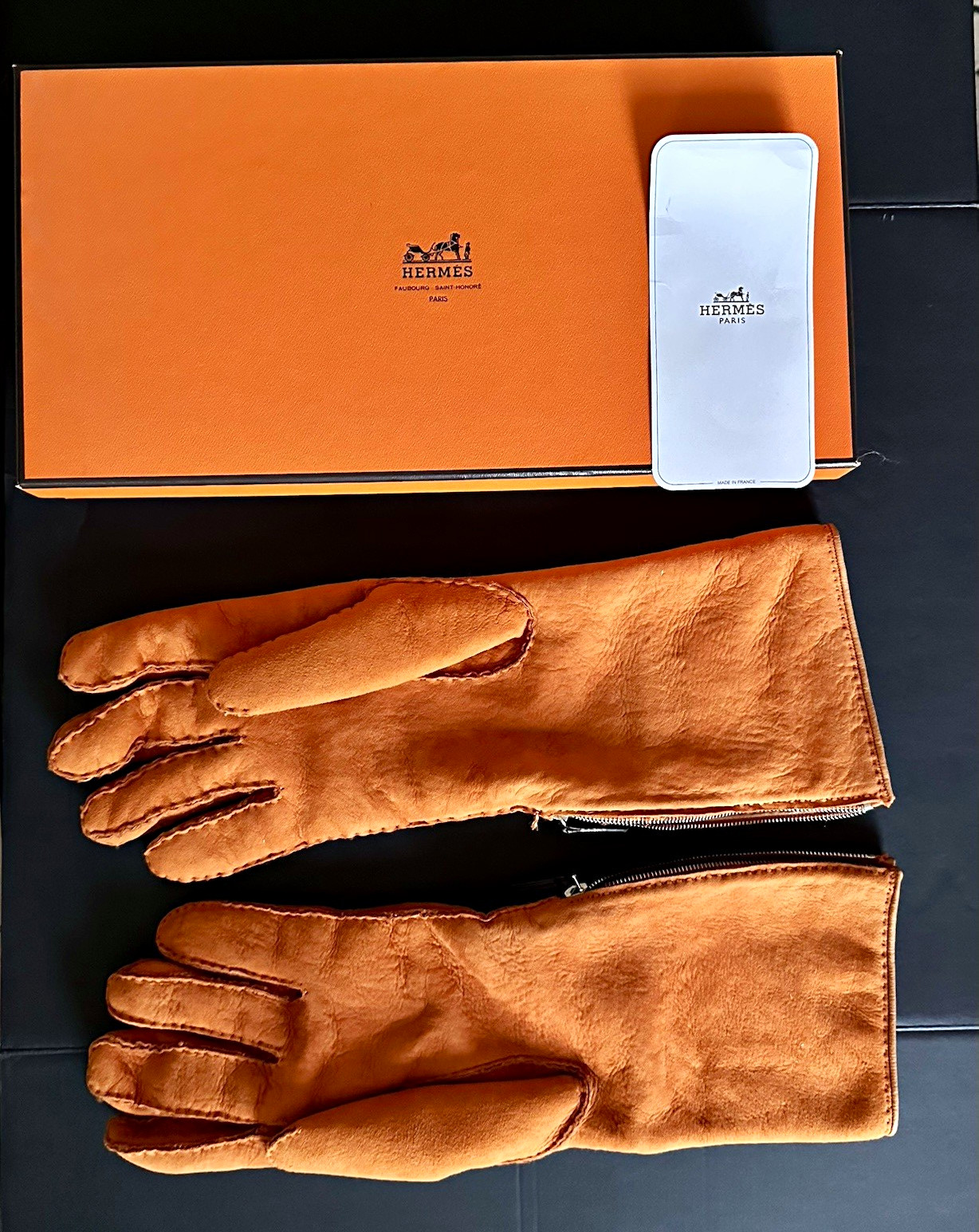 Orange Hermès suede gloves with shearling lining and a zipper closure at the wrist.