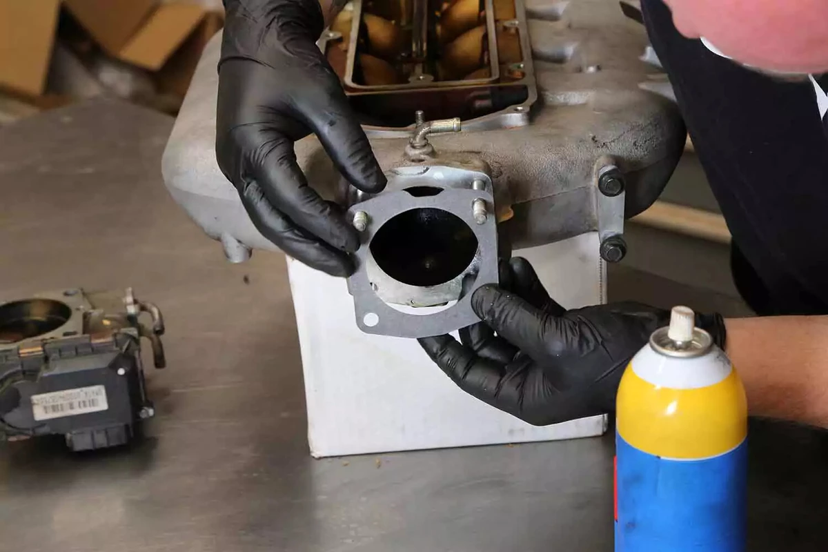 A mechanic slides a new fiber throttle body gasket onto the intake manifold.