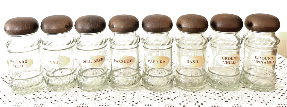 Eight apothecary-style spice bottles topped with hand-turned wooden mushroom caps — the crossover between kitchen utility and cottagecore shelf décor.