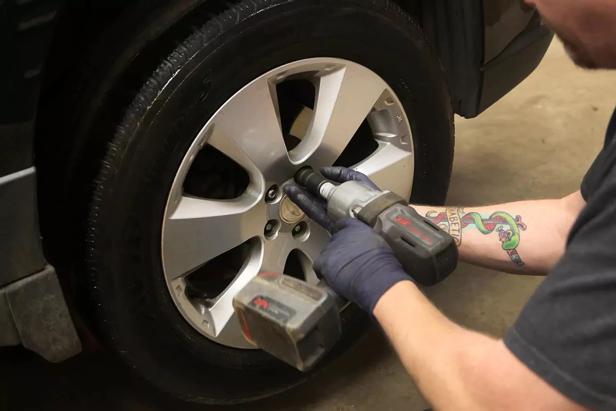 A mechanic uses an Impact gun to remove lug nuts on a wheel.